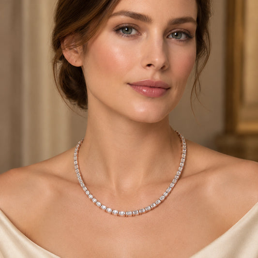 A close-up of a woman wearing a delicate diamond tennis necklace with rose gold settings, styled with a cream off-the-shoulder top against a warm, elegant background.