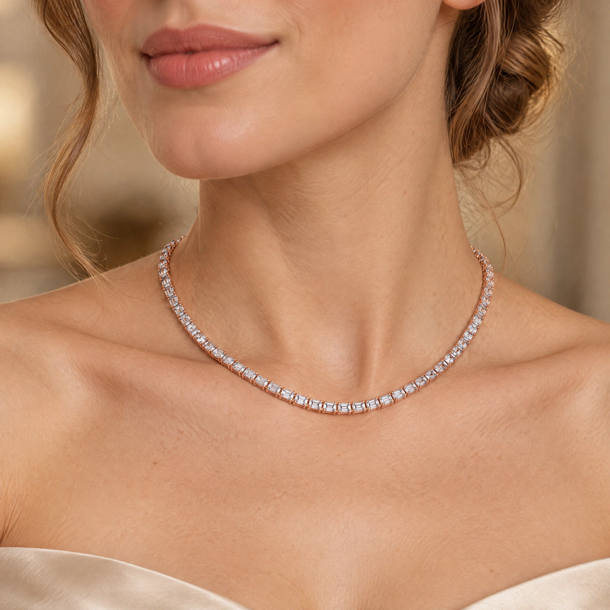 A close-up of a woman wearing a delicate tennis necklace with clear rectangular-cut stones set in a silver-toned metal, shown against her neck and upper chest.